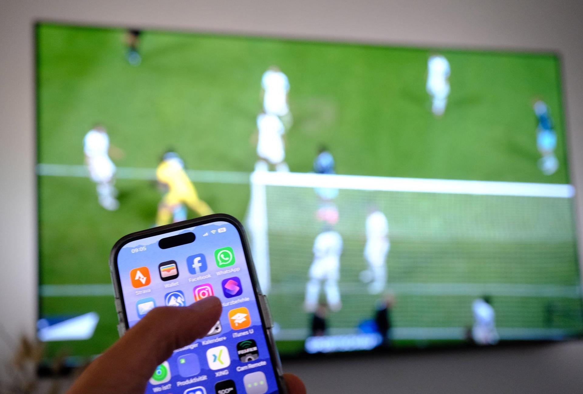 Nebenbei mal daddeln: Während das Fußballspiel läuft, schauen viele Zuschauer nebenbei aufs Handy. (Symbolbild: Bernd Weißbrod/dpa)