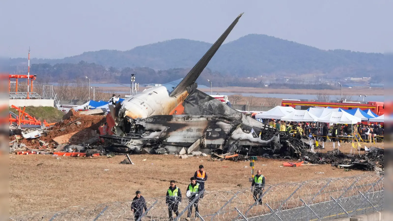 Feuerwehrleute und Rettungskräfte suchen am Wrack des verunglückten Flugzeugs auf dem internationalen Flughafen von Muan nach Opfern.  (Bild: Ahn Young-joon/AP/dpa)