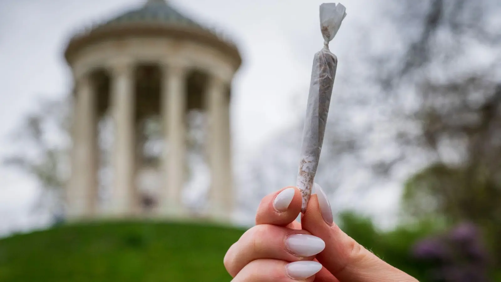 Eine Frau hält einen Joint vor der Kulisse des Monopteros im Englischen Garten. (Bild: Peter Kneffel/dpa)