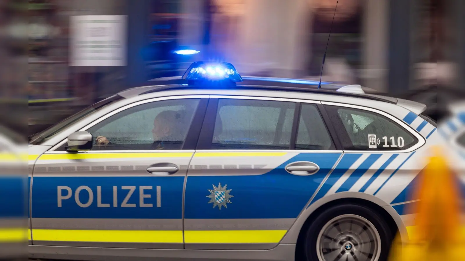 Ein Fahrzeug der bayerischen Polizei fährt mit Blaulicht durch die Innenstadt. (Bild: Peter Kneffel/dpa/Symbolbild)