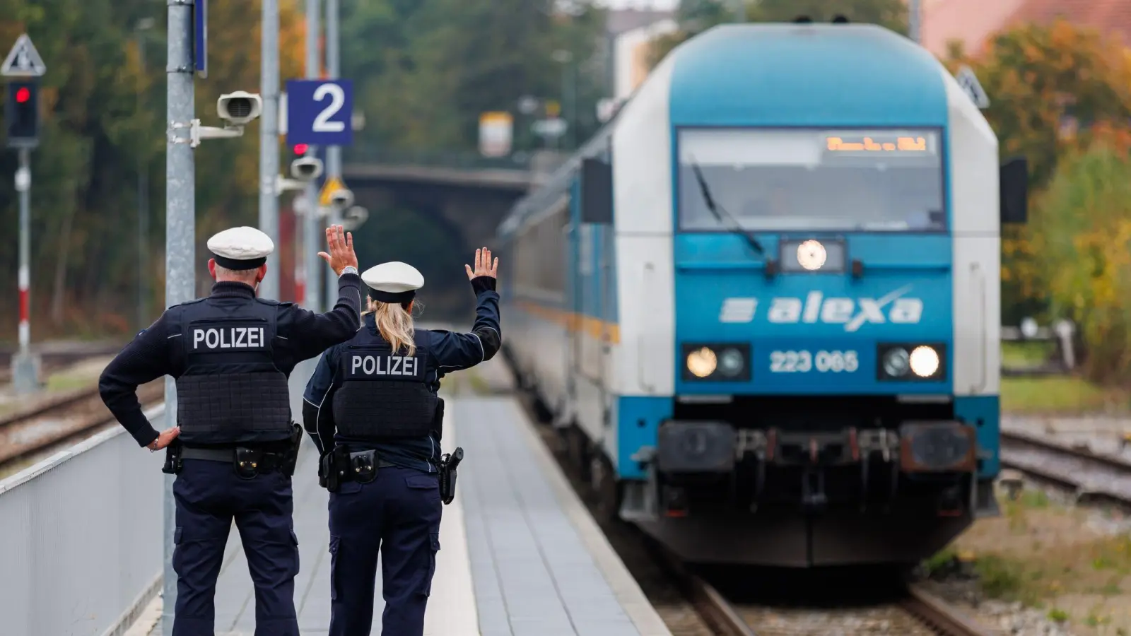 Bundespolizisten weisen per Handzeichen den Lokführer eines Zuges aus Prag in Richtung München darauf hin, dass sie zusteigen werden. (Symbolbild: Daniel Karmann/dpa)