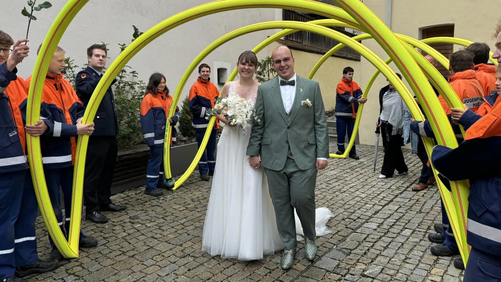 Eine echte Feuerwehr-Hochzeit haben Anja und Florian Schlegel am Samstag gefeiert: Beide Brautleute sind aktiv in der FFW Haselmühl, deren Jugend die Frischvermählten mit einem Ehrenspalier aus neongelben Feuerwehrschläuchen vor der Kirche St. Nikolaus in Theuern empfing. (Bild: Heike Unger)