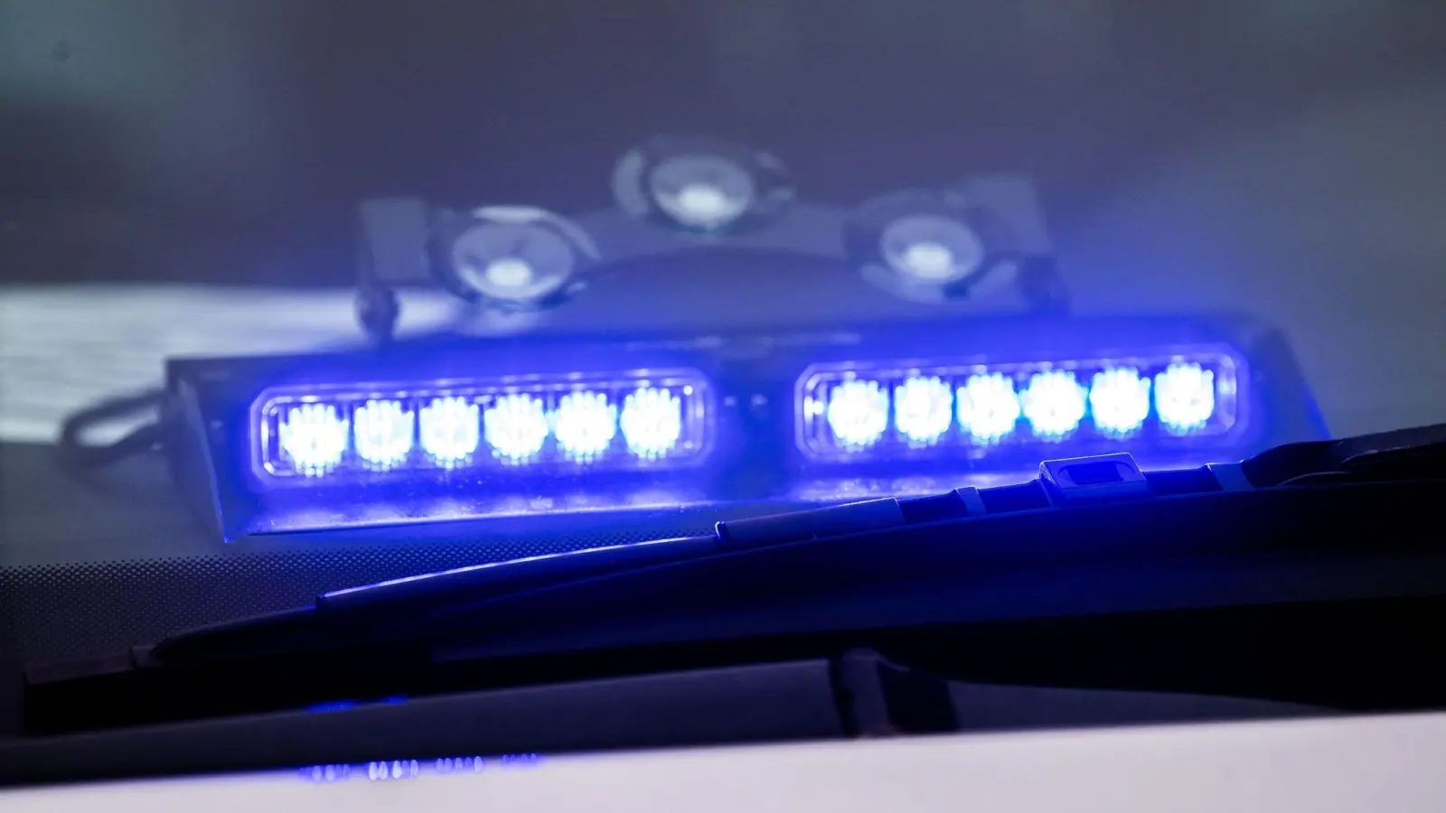 Ein Blaulicht leuchtet unter der Frontscheibe eines Einsatzfahrzeugs der Polizei. (Bild: Lino Mirgeler/dpa/Symbolbild)